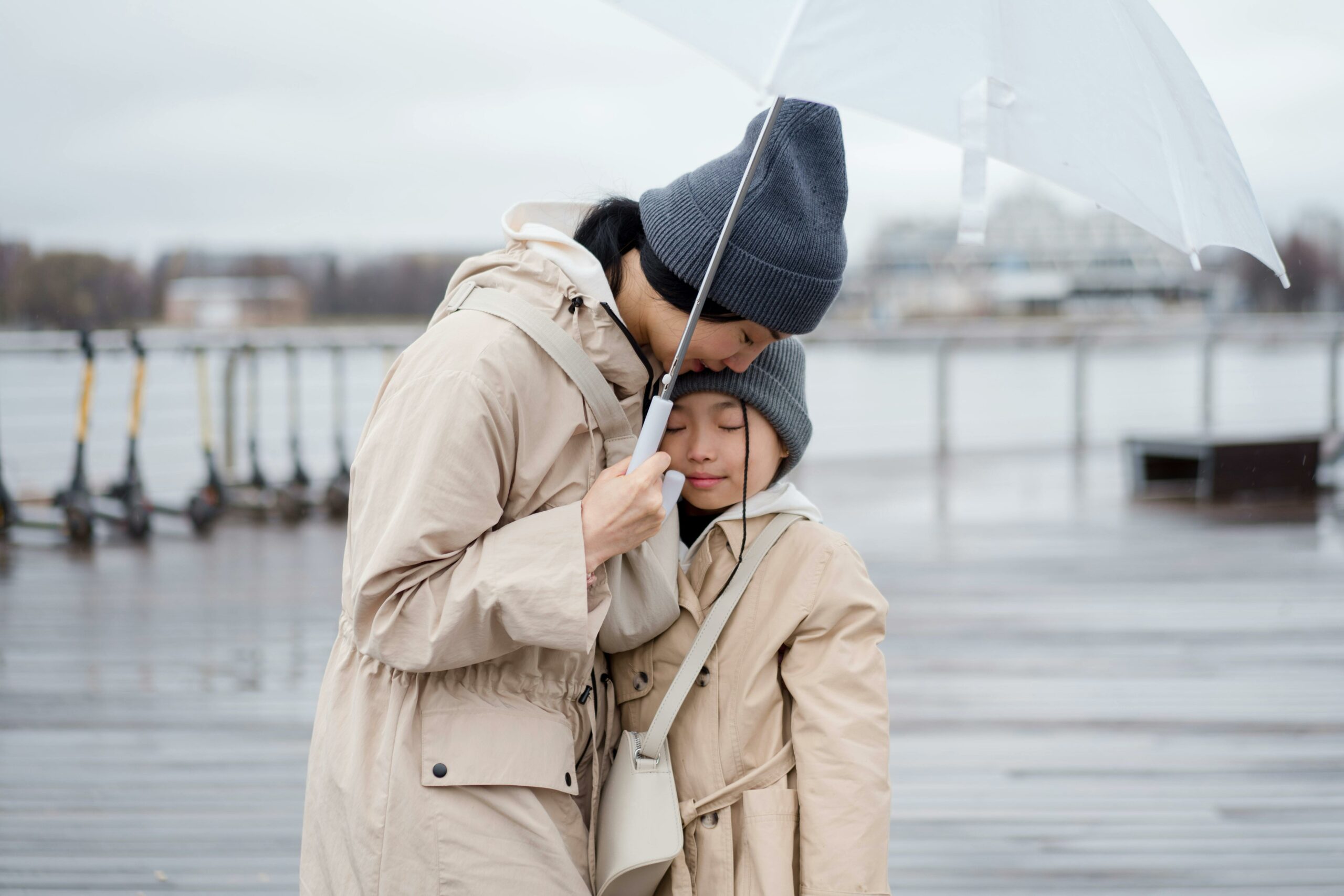 Visuel du billet Sortir sous la pluie en restant stylé représentant une mere et sa fille au bord d'un lac habillée en trench et coupe-vent longtail de couleur beige et un bonnet en laine gris. Photo : Ron Lach